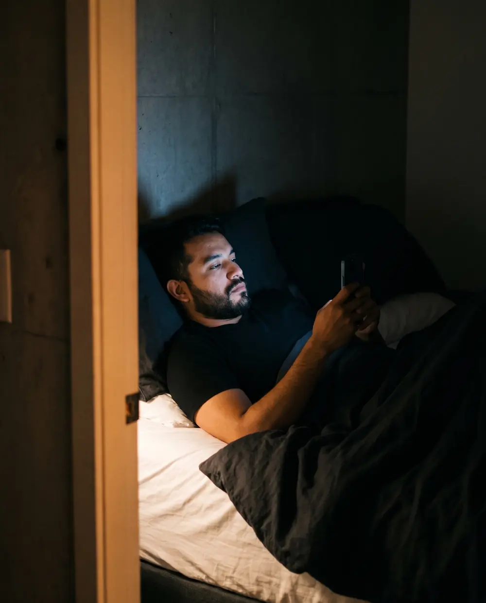 A man lying awake in bed at night, his face lit by his phone
